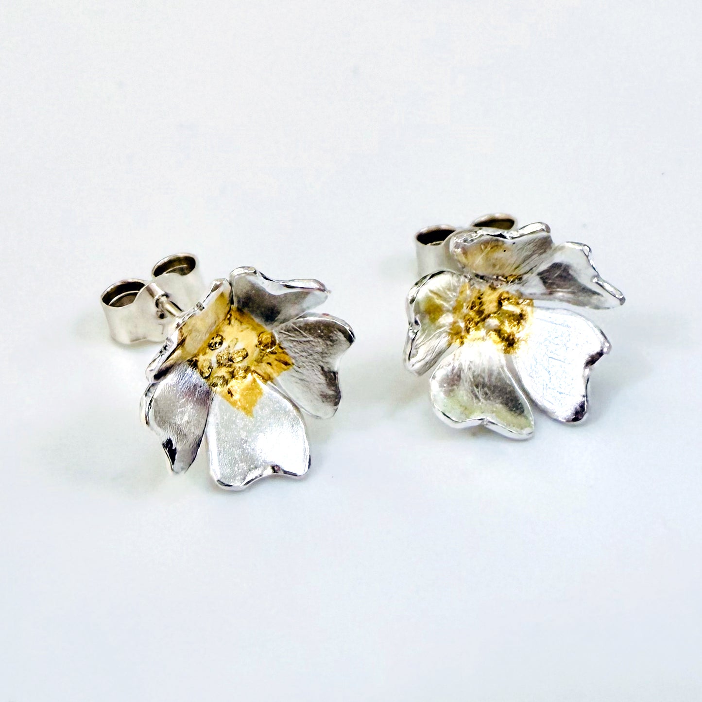 The Expanded Skies Dartmoor Field Rose Studs captures the joyous simple beauty of the field rose, Rosa arvensis, that is seen weaving brightly through the Dartmoor hedgerows and woodland.
Handcrafted in recycled fine silver with recycled 24ct gold accents and recycled sterling silver ear pins and scrolls.