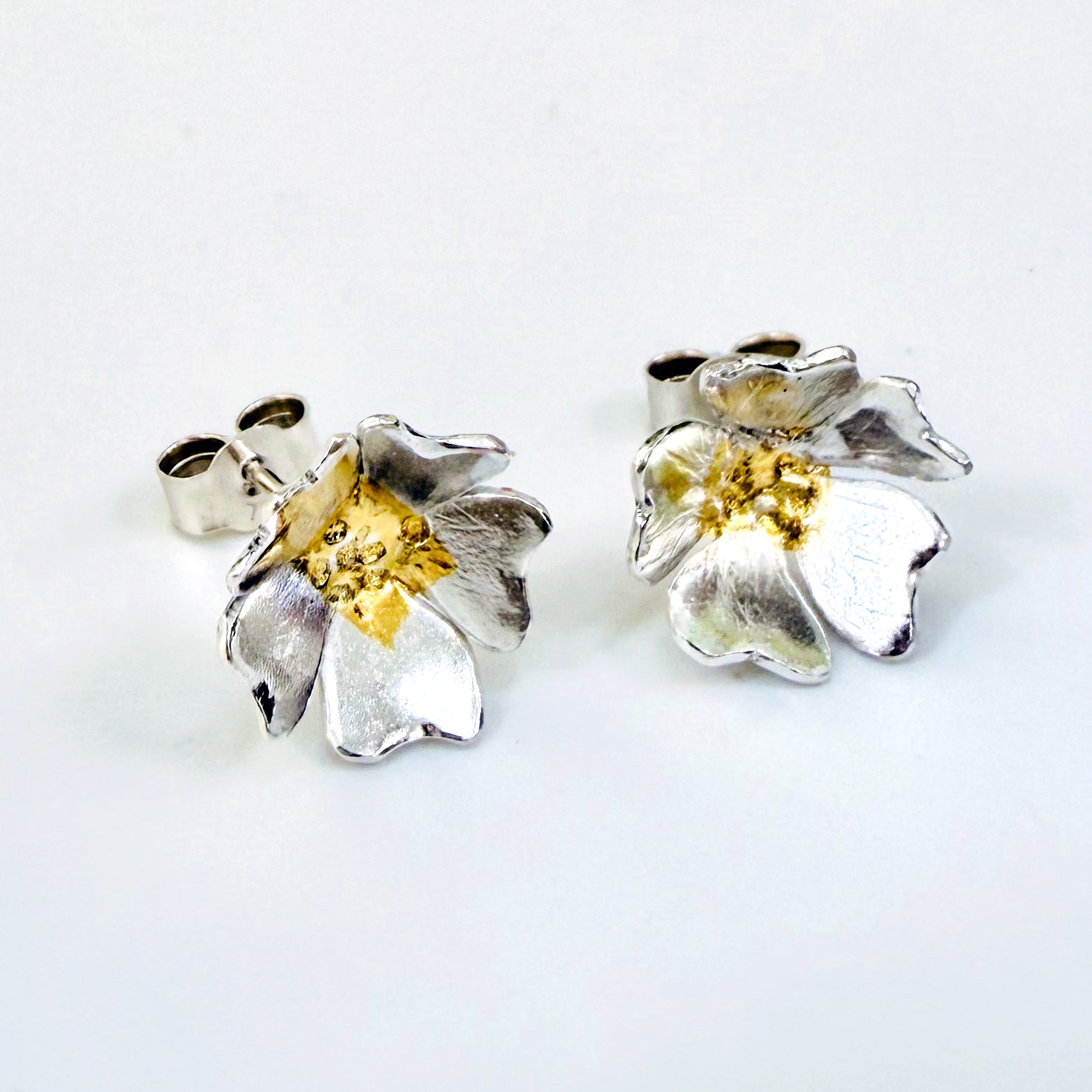 The Expanded Skies Dartmoor Field Rose Studs captures the joyous simple beauty of the field rose, Rosa arvensis, that is seen weaving brightly through the Dartmoor hedgerows and woodland.
Handcrafted in recycled fine silver with recycled 24ct gold accents and recycled sterling silver ear pins and scrolls.