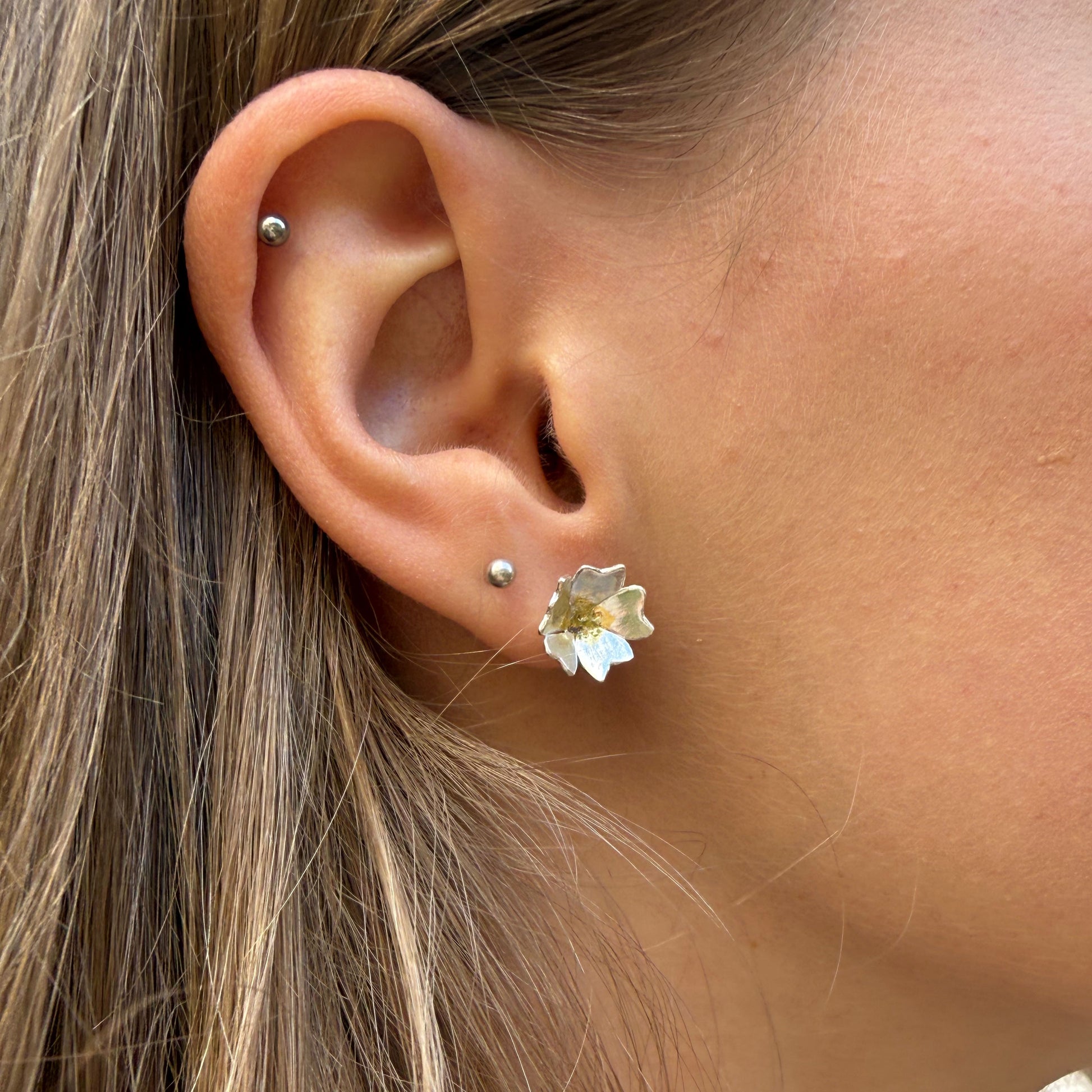 The Expanded Skies Dartmoor Field Rose Studs captures the joyous simple beauty of the field rose, Rosa arvensis, that is seen weaving brightly through the Dartmoor hedgerows and woodland.
Handcrafted in recycled fine silver with recycled 24ct gold accents and recycled sterling silver ear pins and scrolls. Worn by model.
