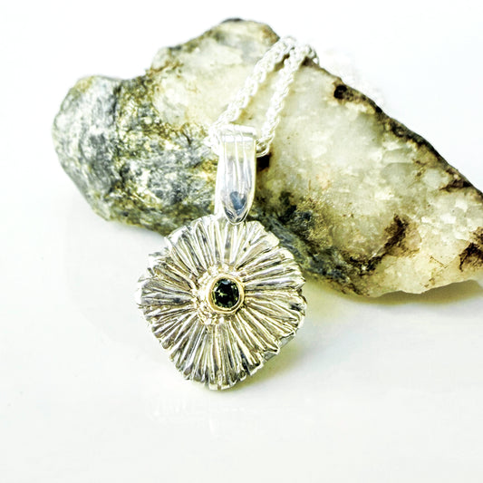 The Expanded Skies Dartmoor Green Daisy Sapphire Necklace in sterling silver and 9ct gold is inspired by the Erigeron Karvinskianus, commonly known as the 'Dartmoor Daisy'. It comes with 16” Italian spiga rolled chain, made from recycled sterling silver. The daisy pendant measures 12mm, the bail measures 6mm, total length 18mm with a depth of 2mm (approx). Each piece is individually saw pierced, hand engraved and unique. The ethically sourced 2.5mm green sapphire is from Queensland, Australia.