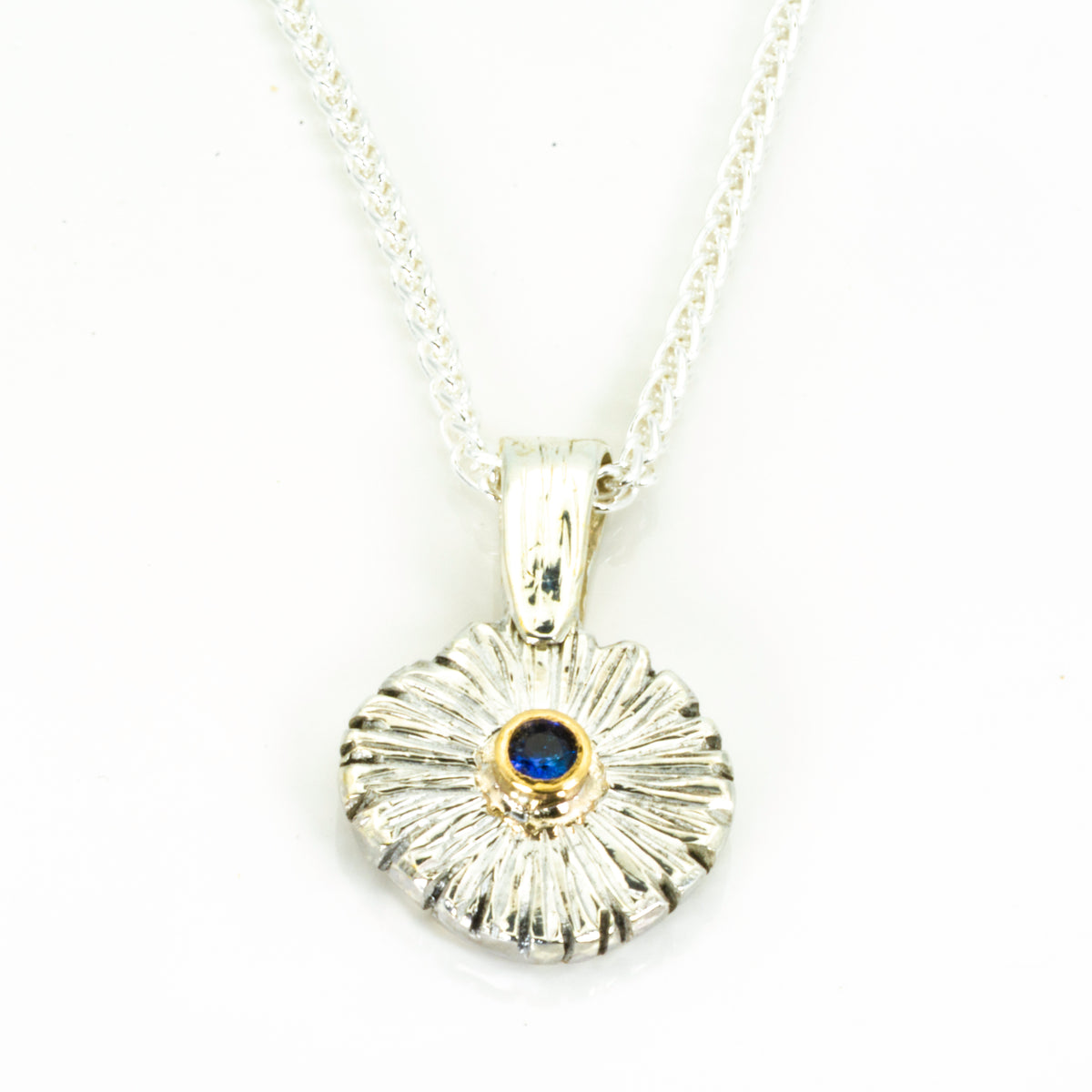 The Expanded Skies Dartmoor Daisy Blue Sapphire Necklace in sterling silver and 9ct gold is inspired by the Erigeron Karvinskianus, commonly known as the 'Dartmoor Daisy'. It comes with 16” Italian spiga rolled chain, made from recycled sterling silver. The daisy pendant measures 12mm, the bail measures 6mm, total length 18mm with a depth of 2mm (approx). Each piece is individually saw pierced, hand engraved and
unique. The ethically sourced 2.5mm is a beautiful brilliant blue, facetted Sri Lankan sapphire,