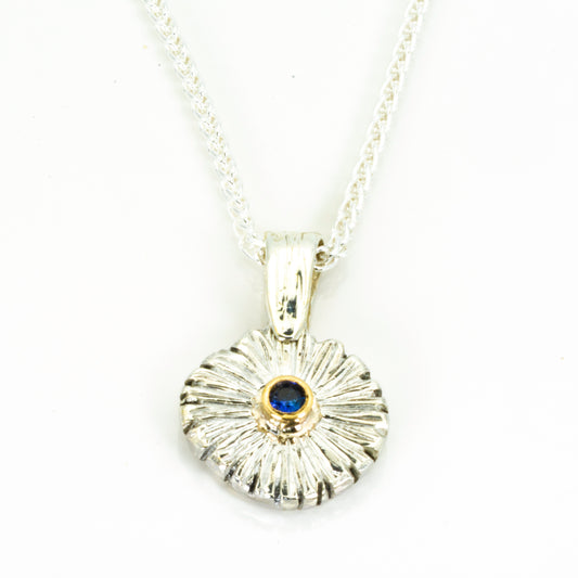 The Expanded Skies Dartmoor Daisy Blue Sapphire Necklace in sterling silver and 9ct gold is inspired by the Erigeron Karvinskianus, commonly known as the 'Dartmoor Daisy'. It comes with 16” Italian spiga rolled chain, made from recycled sterling silver. The daisy pendant measures 12mm, the bail measures 6mm, total length 18mm with a depth of 2mm (approx). Each piece is individually saw pierced, hand engraved and
unique. The ethically sourced 2.5mm is a beautiful brilliant blue, facetted Sri Lankan sapphire,