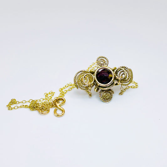 The Expanded Skies Raw Garnet Spiral Filigree Necklace has a beautiful raw Norwegian garnet set in 9ct gold. The garnet is set in a distinctive completely handcrafted 9ct gold filigree and claw setting. It features the neolithic symbol of the spiral, representing the life force and the cycles of life. This is a unique piece, one-of-a-kind. Handcrafted on the edge of Dartmoor and made from high quality recycled gold, Hallmarked by the London Assay Office.