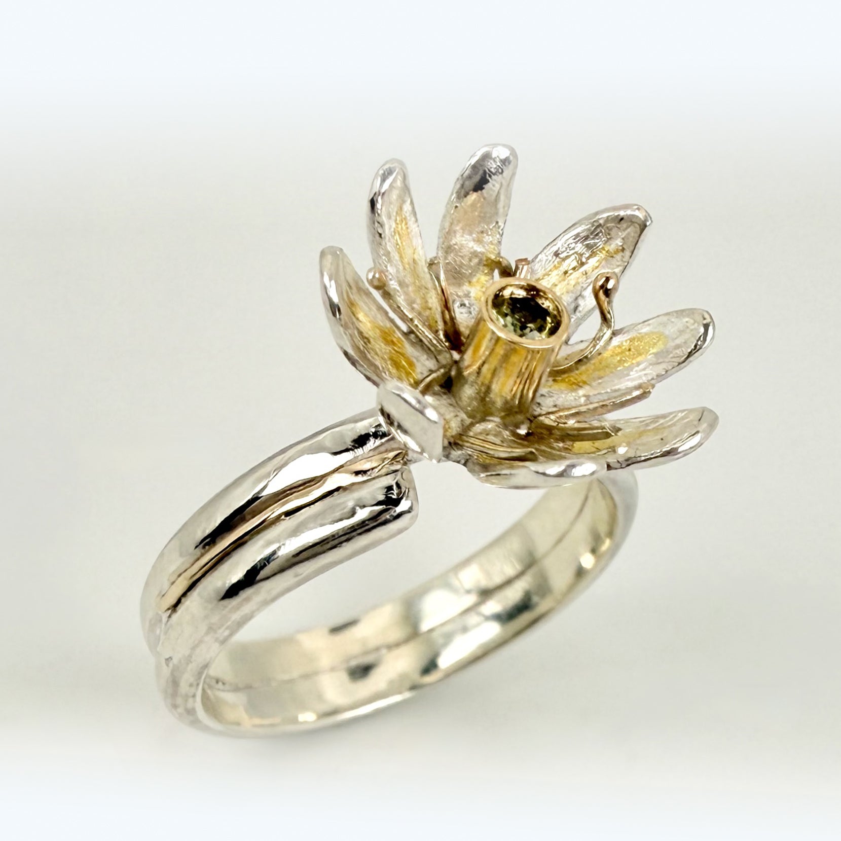 Expanded Skies Dartmoor Celandine Sapphire Ring celebrates the beauty of the waysides and meadows, radiant with wild yellow celandines (Ficaria verna).

The ring is totally handcrafted on the edge of Dartmoor. The band is made from sterling silver, inlaid on the shoulders with 9ct gold.

The flower is made from fine silver with 24ct gold accents fused to the surface of the petals. The celandine has a 9ct gold setting for the beautiful ethically sourced yellow-green sapphire, that really captures the colours