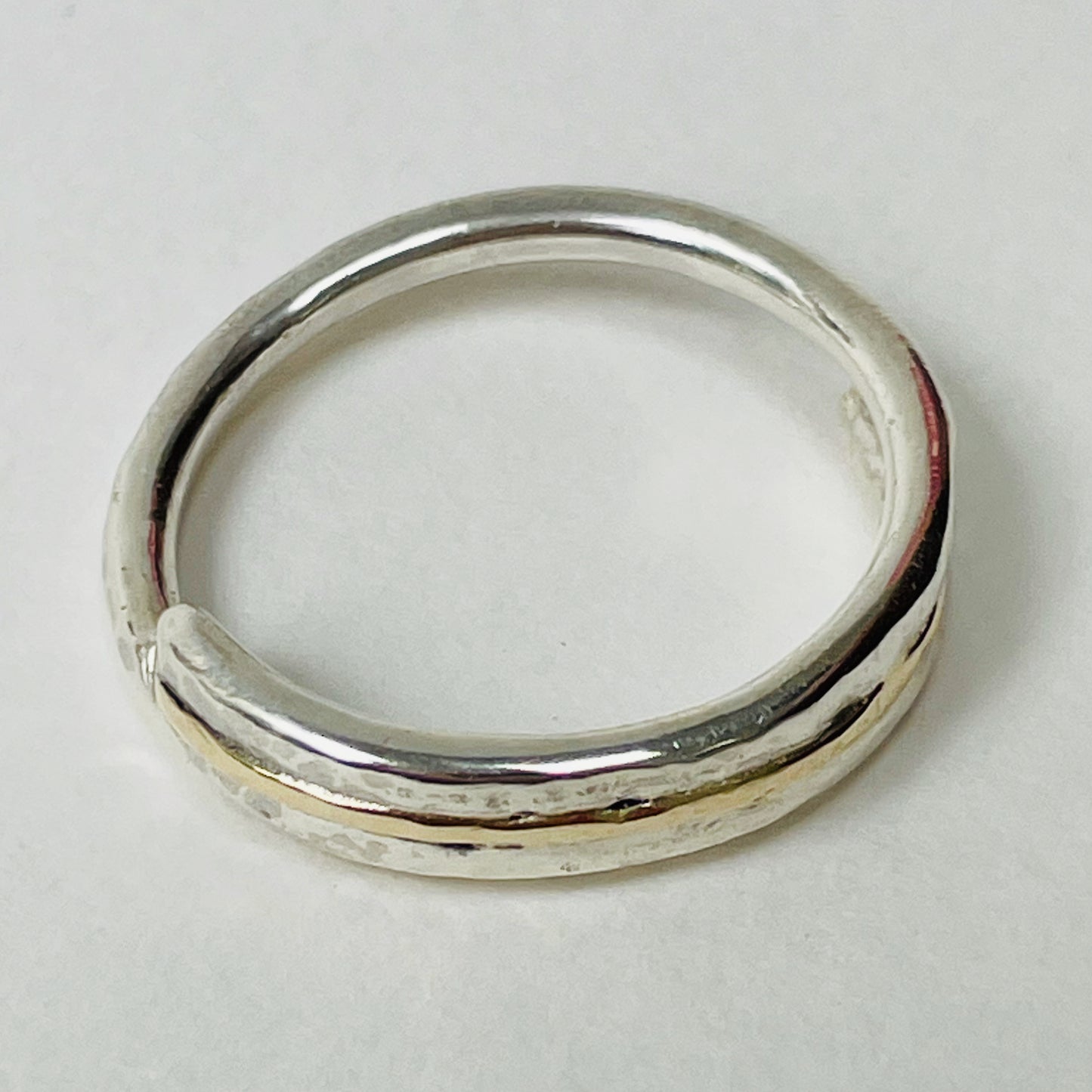 The Dartmoor Dart Valley Hammered Ring, inlaid with 9ct Gold, is inspired by the River Dart, that viewed from high on top of granite moorland, glints and snakes through the steep sides of the deeply wooded valley.  The hammered band is handcrafted from a single band of sold sterling recycled silver at back that flows into a recycled 9ct gold band at the front, flanked by two silver bands.  Wear everyday, perfect as a wedding ring or to accompany any outfit, understated, beautiful.