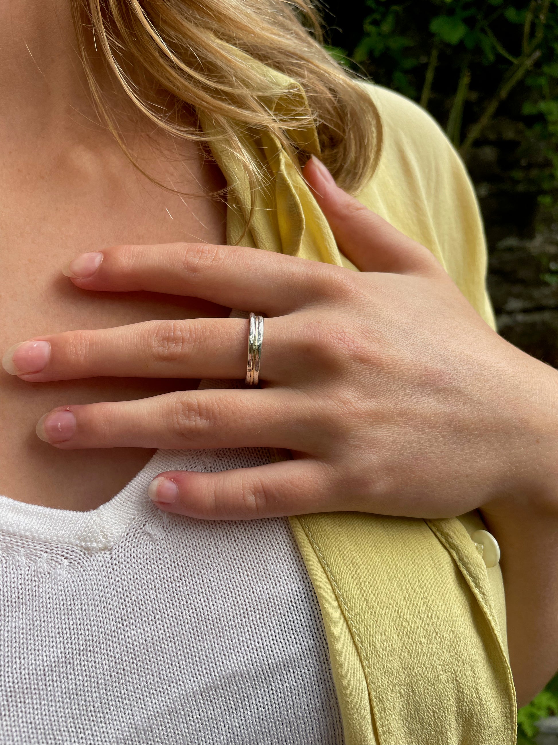 Woman wearing The Dartmoor Dart Valley Hammered Ring, inlaid with 9ct Gold, is inspired by the River Dart, that viewed from high on top of granite moorland, glints and snakes through the steep sides of the deeply wooded valley.  The hammered band is handcrafted from a single band of sold sterling recycled silver at back that flows into a recycled 9ct gold band at the front, flanked by two silver bands.  Wear everyday, perfect as a wedding ring or to accompany any outfit, understated, beautiful.