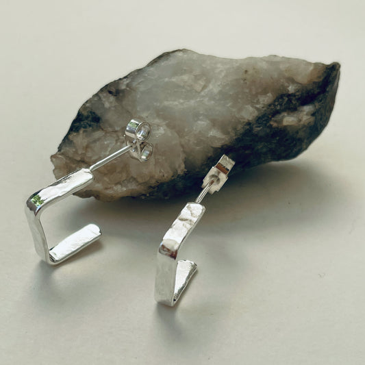 Evoking the angular boulders of Dartmoor, the Expanded Skies, Dartmoor Square Hoop Earrings are handcrafted from solid recycled sterling silver with a recycled sterling silver pin and scroll back. Simple and elegant, with a hammered finish they can be worn everyday for any occasion.