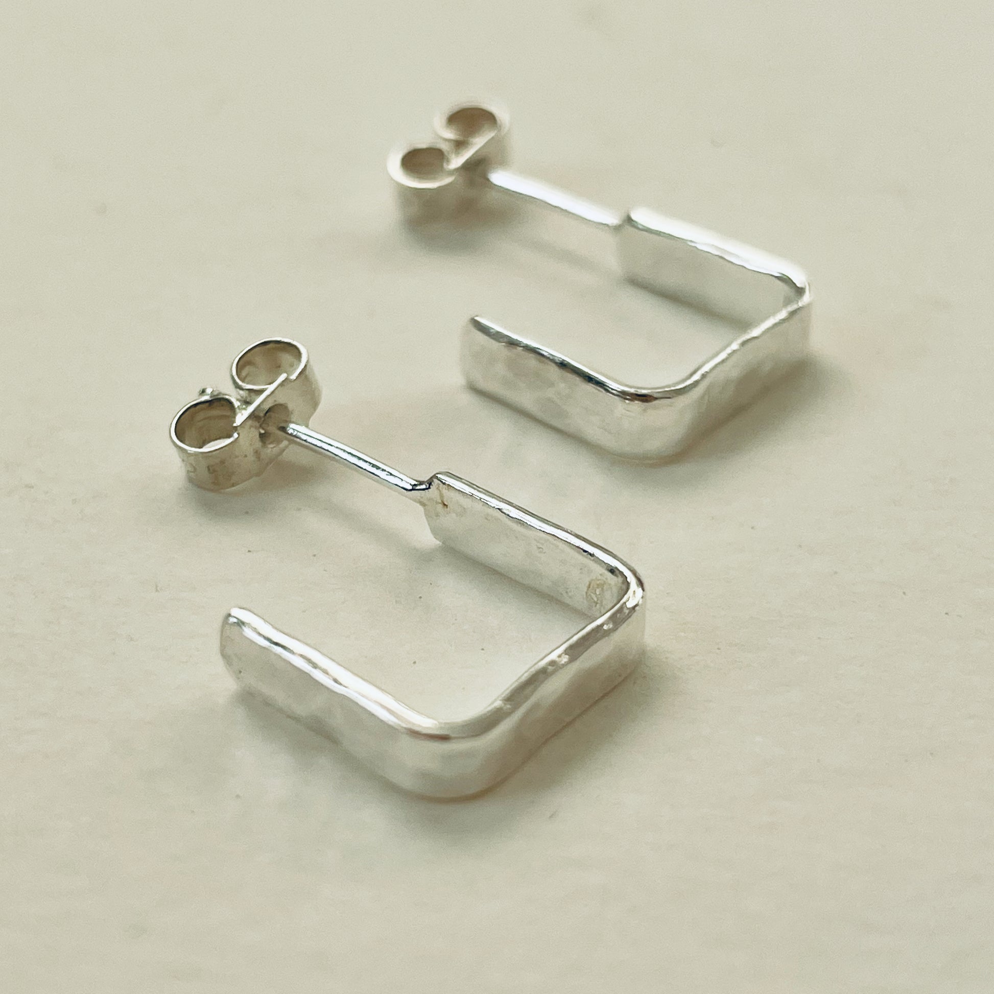 Evoking the angular boulders of Dartmoor, the Expanded Skies, Dartmoor Square Hoop Earrings are handcrafted from solid recycled sterling silver with a recycled sterling silver pin and scroll back. Simple and elegant, with a hammered finish they can be worn everyday for any occasion.