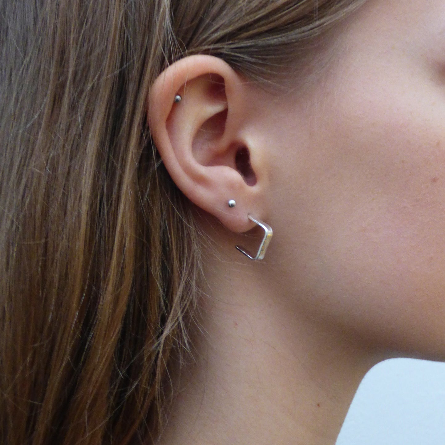 Evoking the angular boulders of Dartmoor, the Expanded Skies, Dartmoor Square Hoop Earrings are handcrafted from solid recycled sterling silver with a recycled sterling silver pin and scroll back. Simple and elegant, with a hammered finish they can be worn everyday for any occasion.