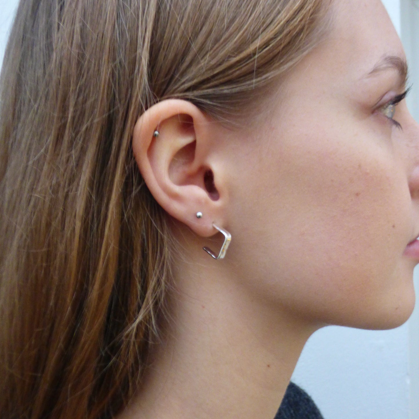 Evoking the angular boulders of Dartmoor, the Expanded Skies, Dartmoor Square Hoop Earrings are handcrafted from solid recycled sterling silver with a recycled sterling silver pin and scroll back. Simple and elegant, with a hammered finish they can be worn everyday for any occasion.