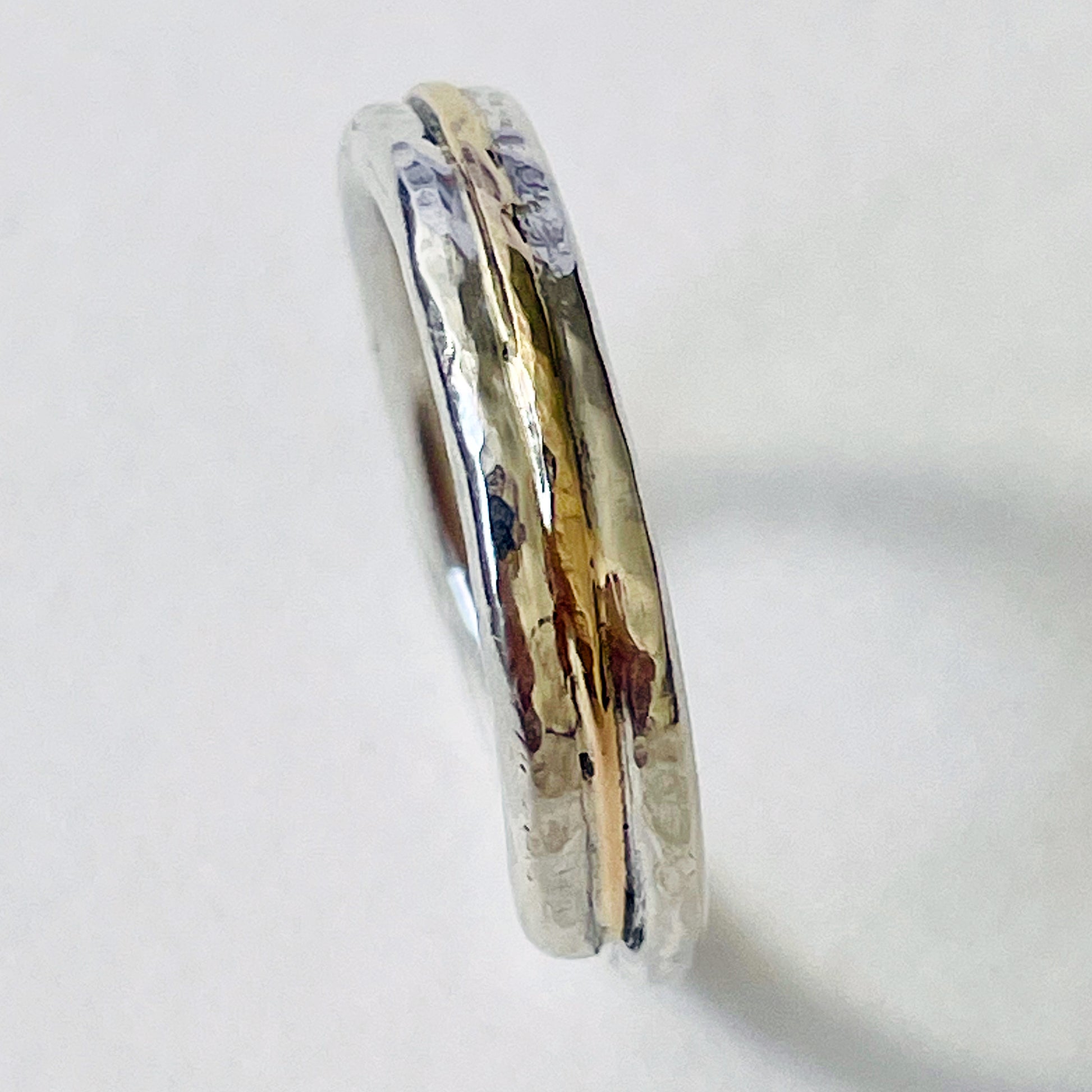 The Dartmoor Dart Valley Hammered Ring, inlaid with 9ct Gold, is inspired by the River Dart, that viewed from high on top of granite moorland, glints and snakes through the steep sides of the deeply wooded valley.  The hammered band is handcrafted from a single band of sold sterling recycled silver at back that flows into a recycled 9ct gold band at the front, flanked by two silver bands.  Wear everyday, perfect as a wedding ring or to accompany any outfit, understated, beautiful.