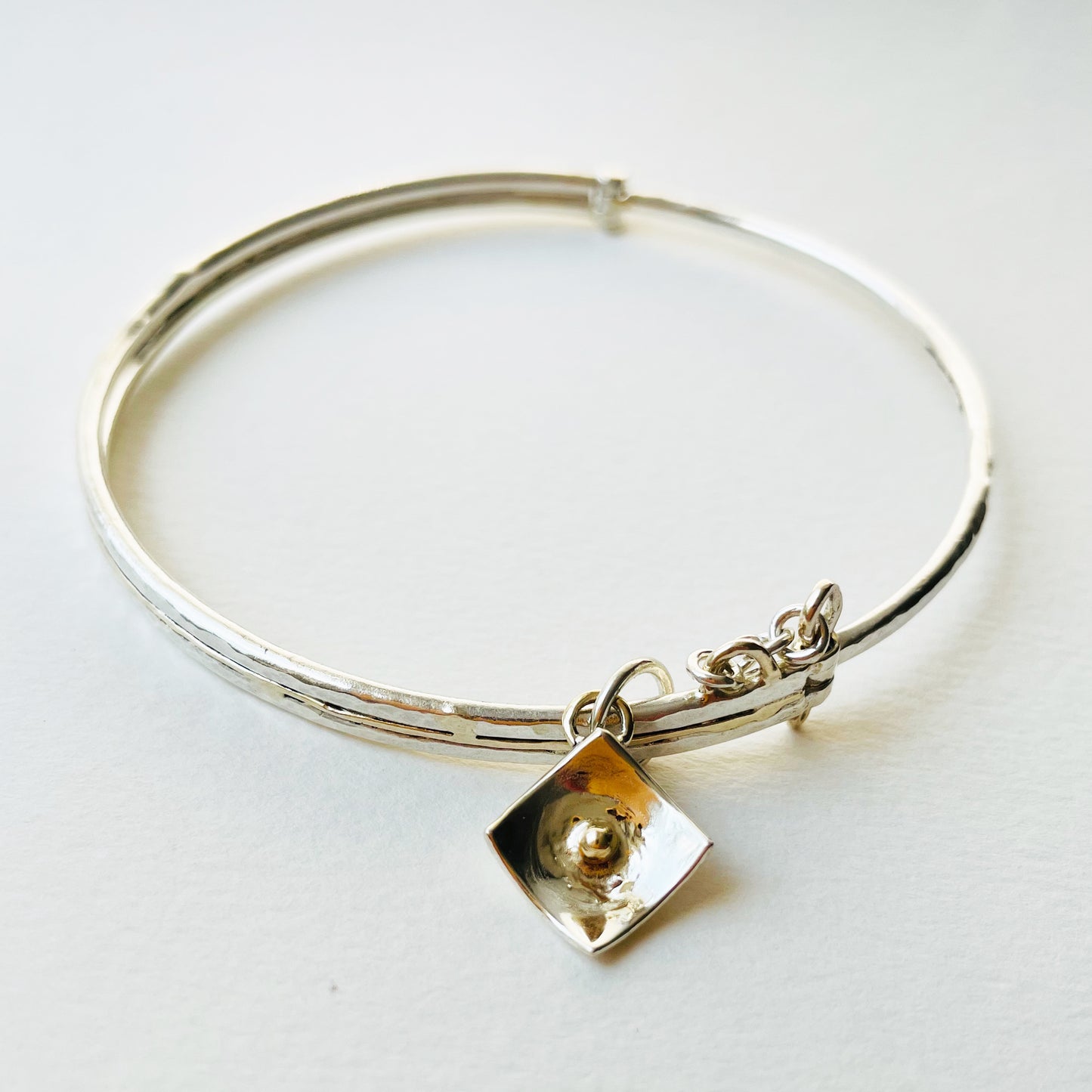 Expanded Skies Hinged Charm Bangle is made from high quality recycled sterling silver inlaid with recycled 9ct gold with a textured hammered finish that reflects the light. Understated and beautiful, it can be worn every day or for special occasions. The hinged bangle  The totally handcrafted hinged bangle has a choice of charms, some set with beautiful ethically sourced Sri Lankan sapphires, including stars, heart,  and a Vesica Piscis.