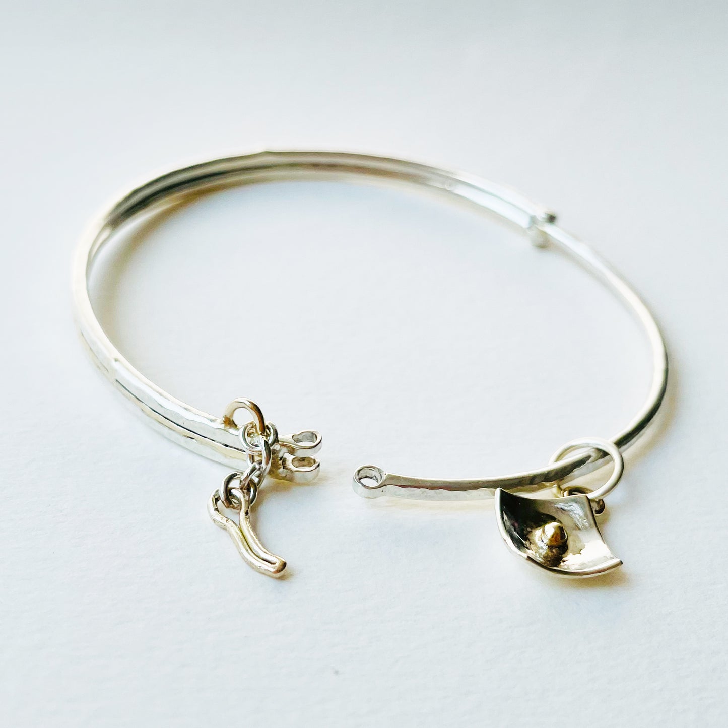 Expanded Skies Hinged Charm Bangle is made from high quality recycled sterling silver inlaid with recycled 9ct gold with a textured hammered finish that reflects the light. Understated and beautiful, it can be worn every day or for special occasions. The hinged bangle  The totally handcrafted hinged bangle has a choice of charms, some set with beautiful ethically sourced Sri Lankan sapphires, including stars, heart,  and a Vesica Piscis.