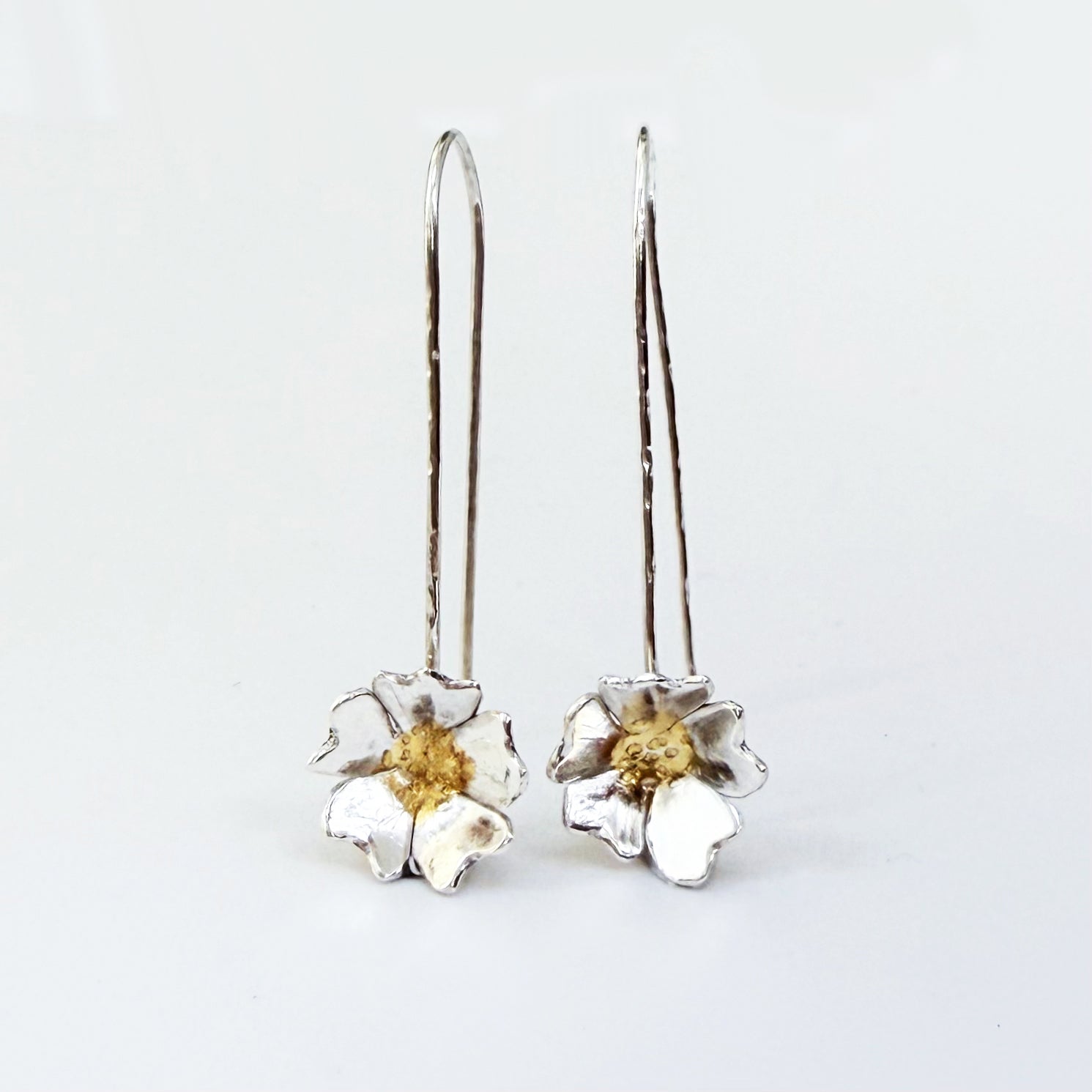 The Expanded Skies Dartmoor Field Rose Drop Earrings capture the joyous simple beauty of the field rose, Rosa arvensis, that is seen weaving brightly through the Dartmoor hedgerows and woodland. Hand pierced and formed in recycled fine silver with recycled 24ct gold accents and recycled sterling silver ear wires. 