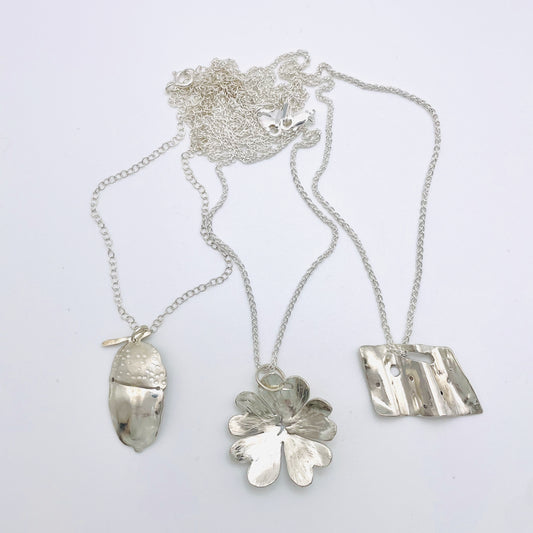 Ashburton Jewellery School Create a silver pendant in this fun workshop on Saturday 12 July 2025. Picture of acorn, primrose and abstract silver pendants and chains.