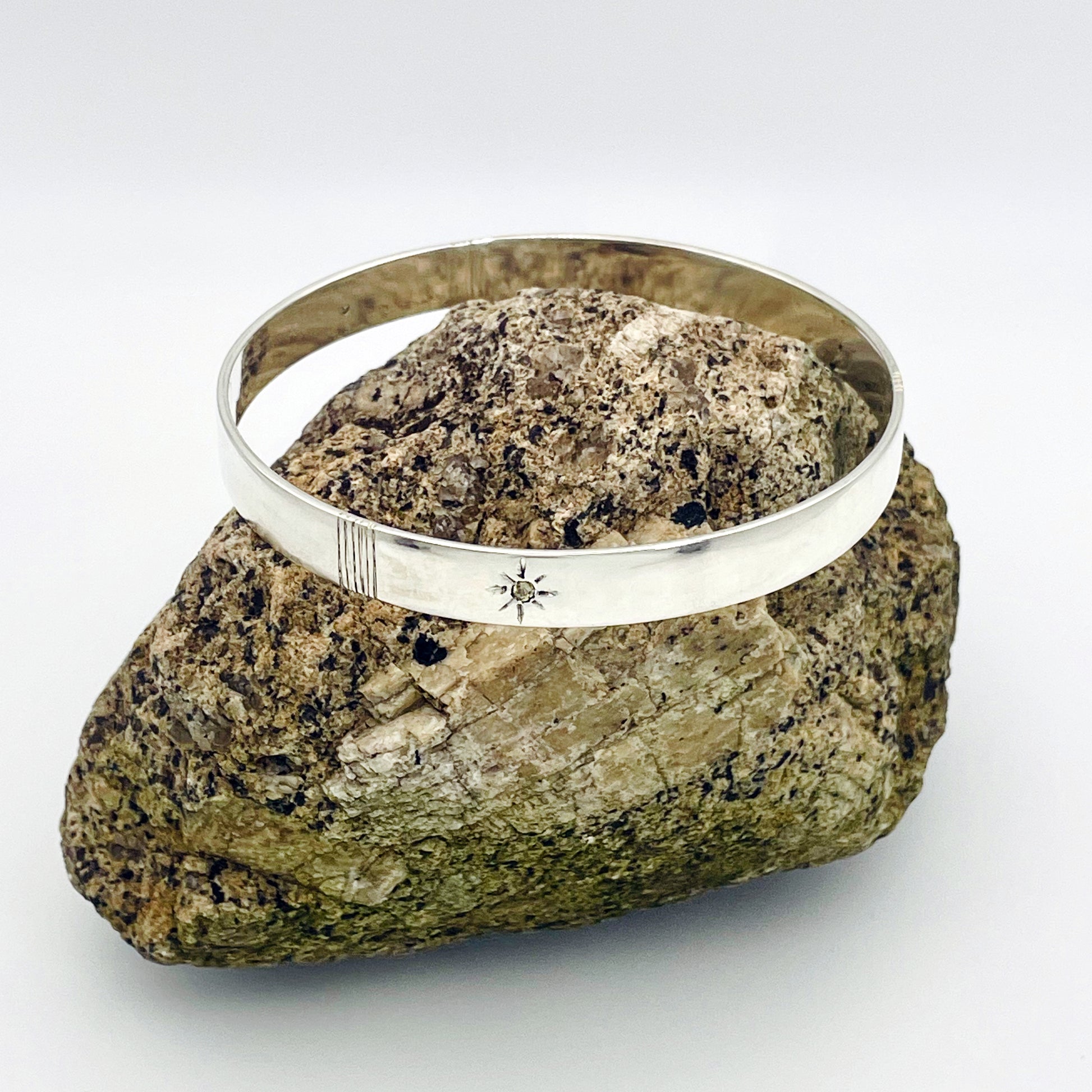Expanded Skies Yellow Sapphire Star Set Bangle evokes the stars that shine bright in the dark skies on Dartmoor.

Three yellow Sri Lankan sapphires are star set with hand engraved rays in the signature hand-drawn aesthetic. The bangle is totally handcrafted on the edge of Dartmoor in high quality recycled sterling silver. For men and women, simple, beautiful.