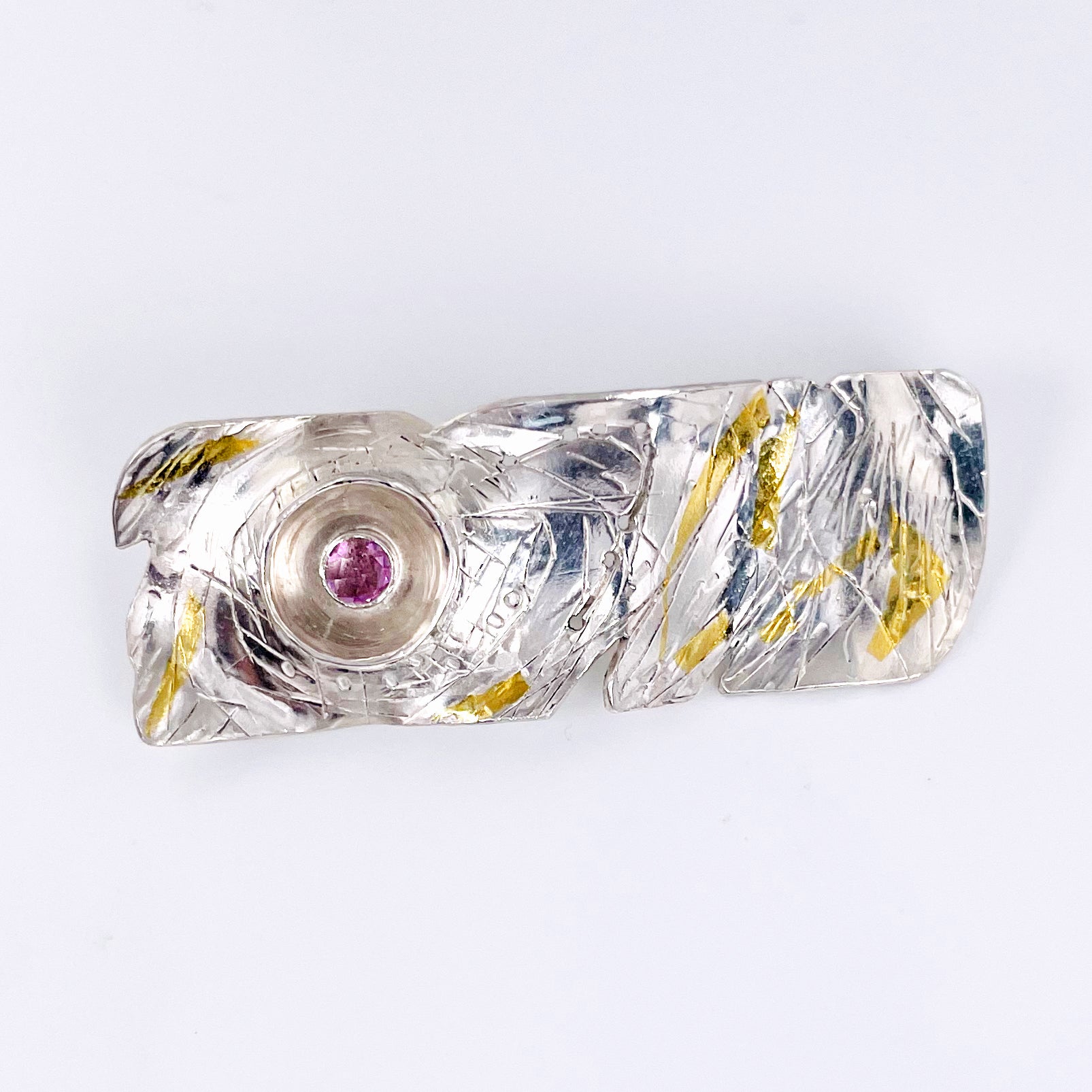 The Expanded Skies Expanded Skies Dartmoor Sun and Stars Pink Sapphire Brooch is inspired by the rising sun and the emerging stars in Dartmoor skies. Created with hand engraving and gold accents with a beautiful pink sapphire.