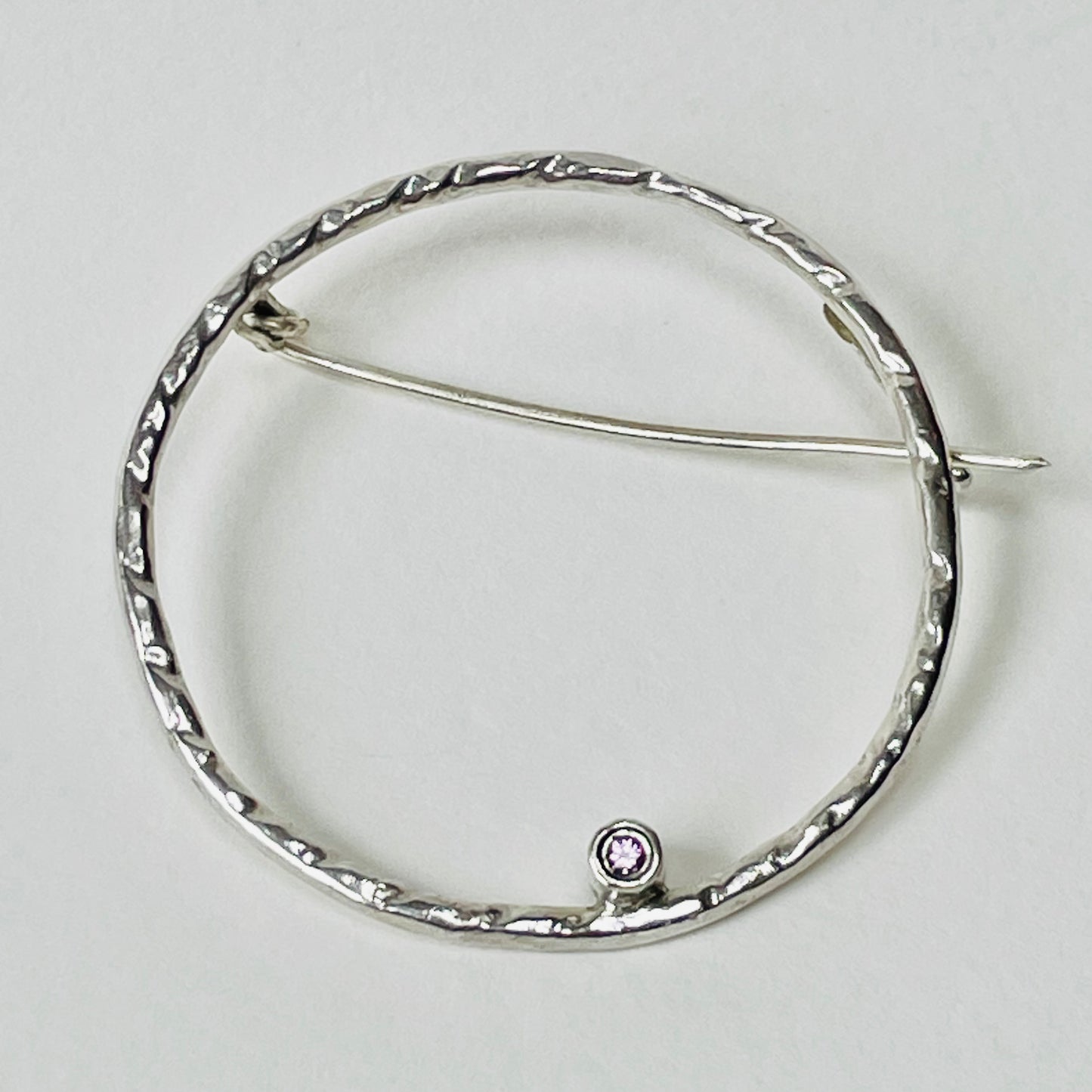 The Pink Moon Sapphire Brooch is totally handcrafted. Featuring a beautiful 2mm ethically mined pink Sri Lankan sapphire set in high quality recycled sterling silver (925) hoop.   The brooch adds a touch of glamour to casual clothes or formal wear. It can be worn as part of a set with the Full Moon White Sapphire Pendant.  Dimensions:  The brooch hoop has 35mm diameter 